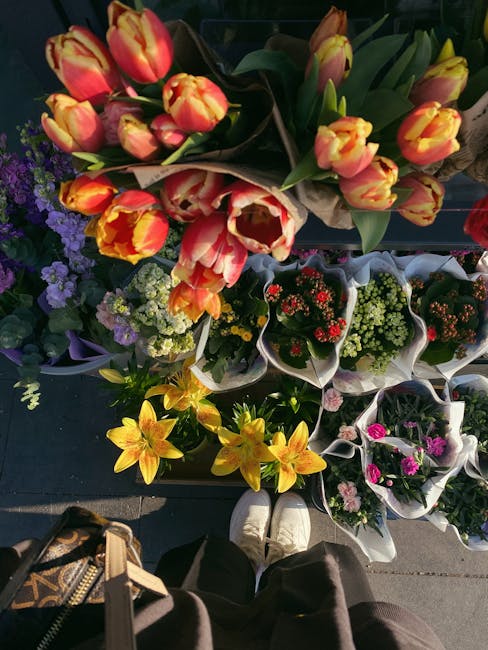 A top-down view of a variety of floral arrangements displayed at a flower shop, featuring a bouquet of yellow lilies and a larger bouquet of multicoloured tulips with shades of yellow and red, wrapped